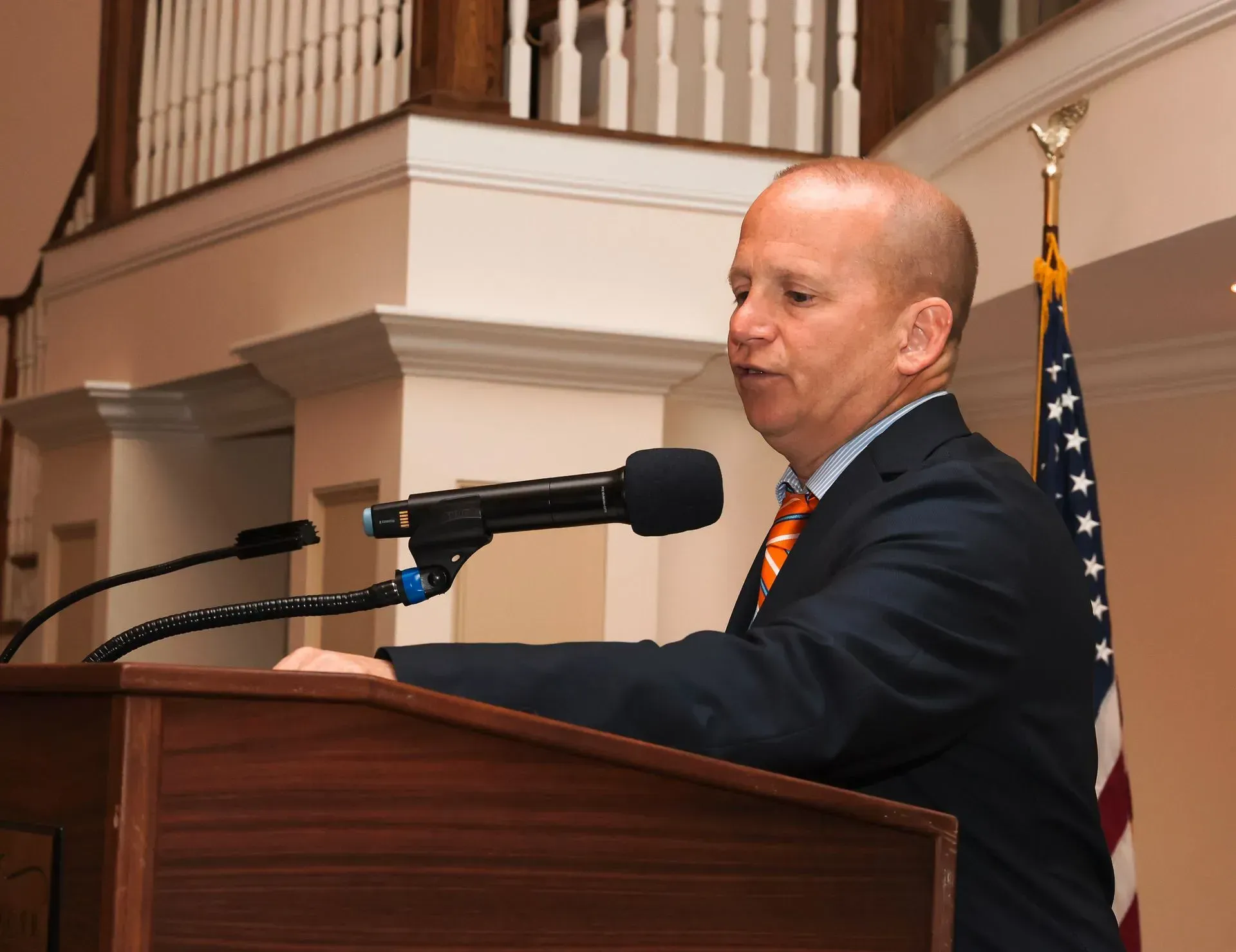 a man in a suit and tie stands at a podium speaking into a microphone