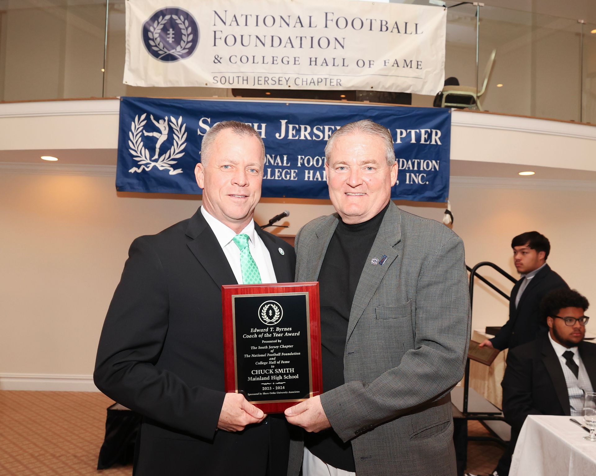 Two men holding a plaque in front of a banner that says national football foundation south jersey chapter