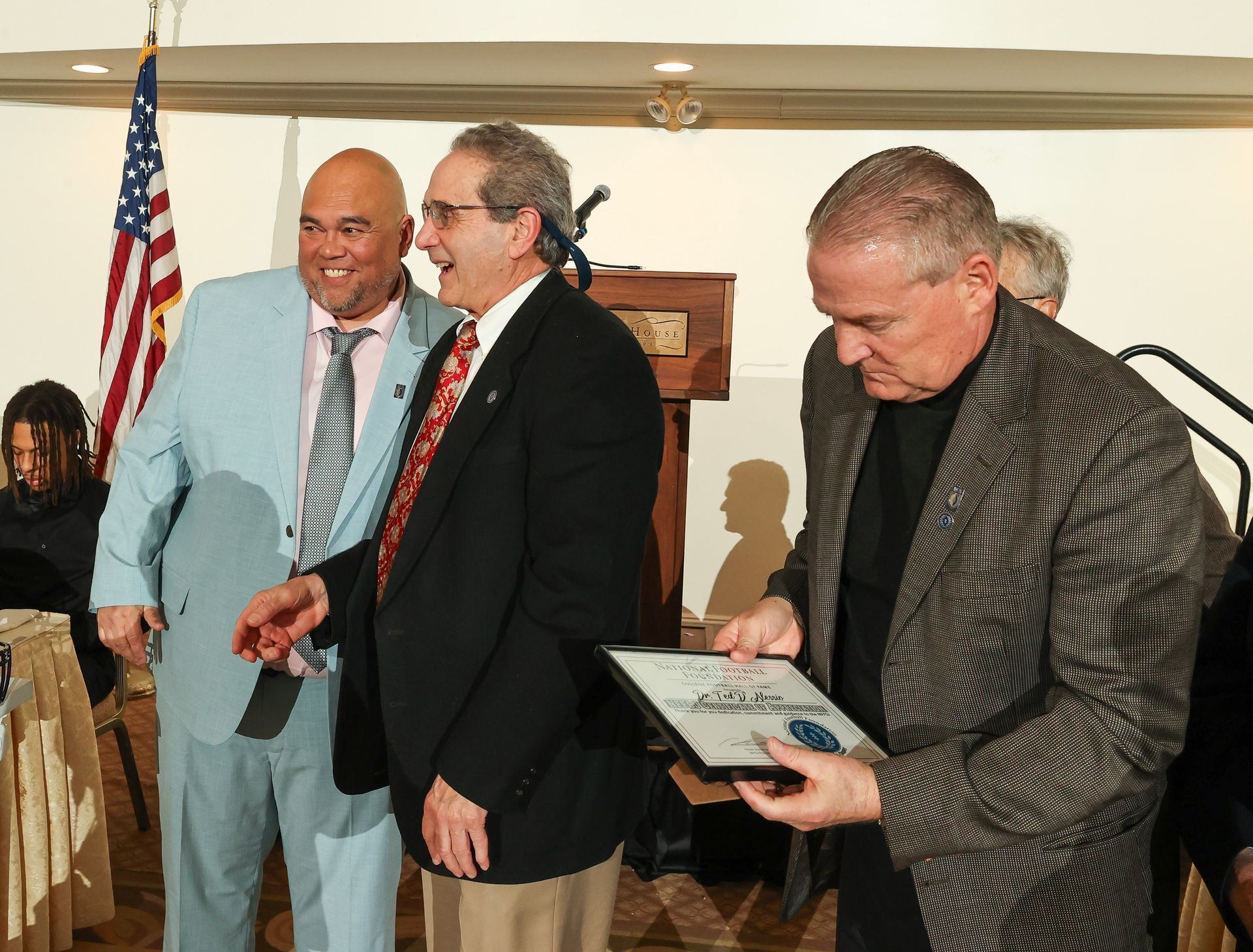 Three men in suits and ties are standing in front of an american flag