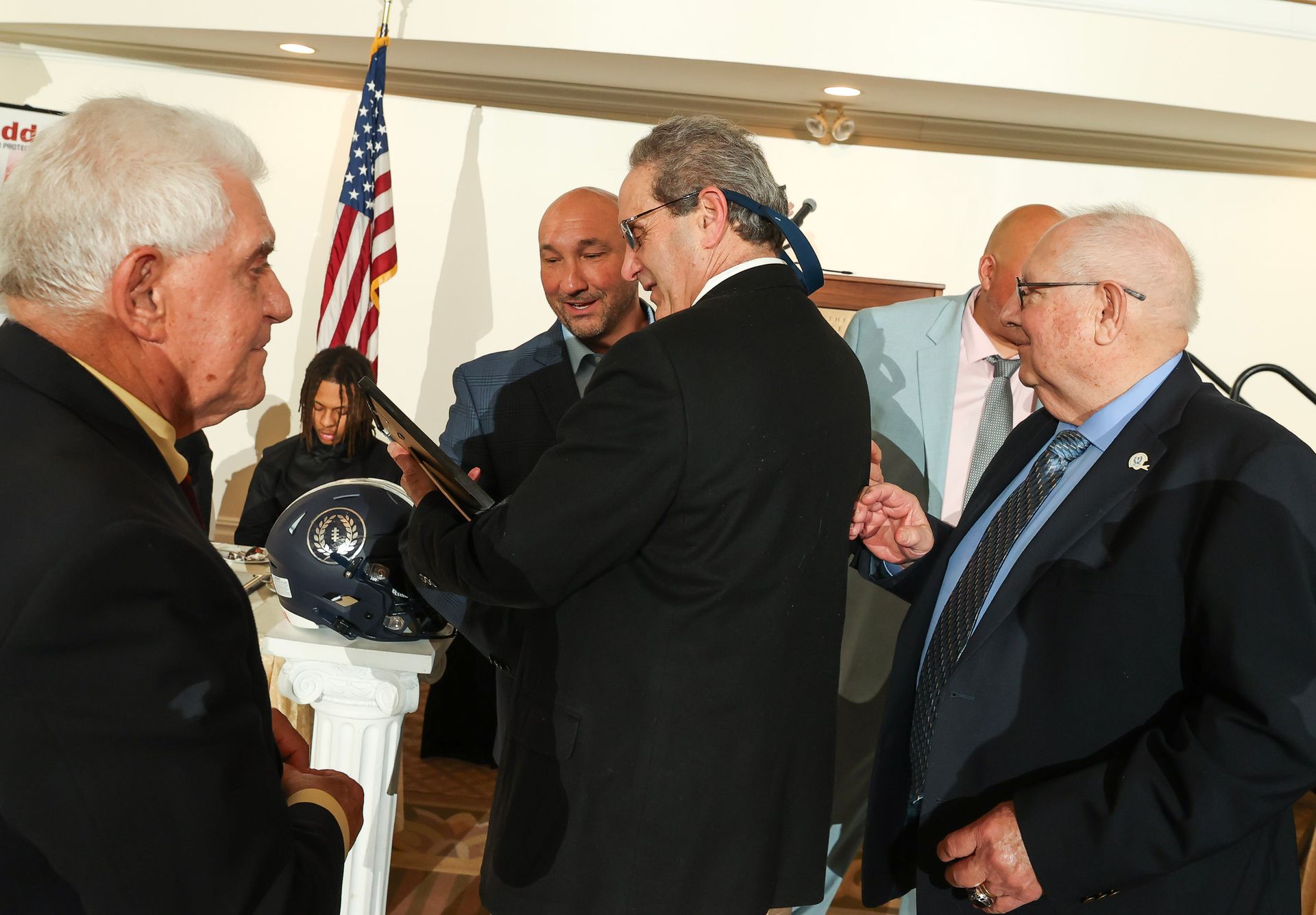 A group of men are standing around a table with an american flag in the background