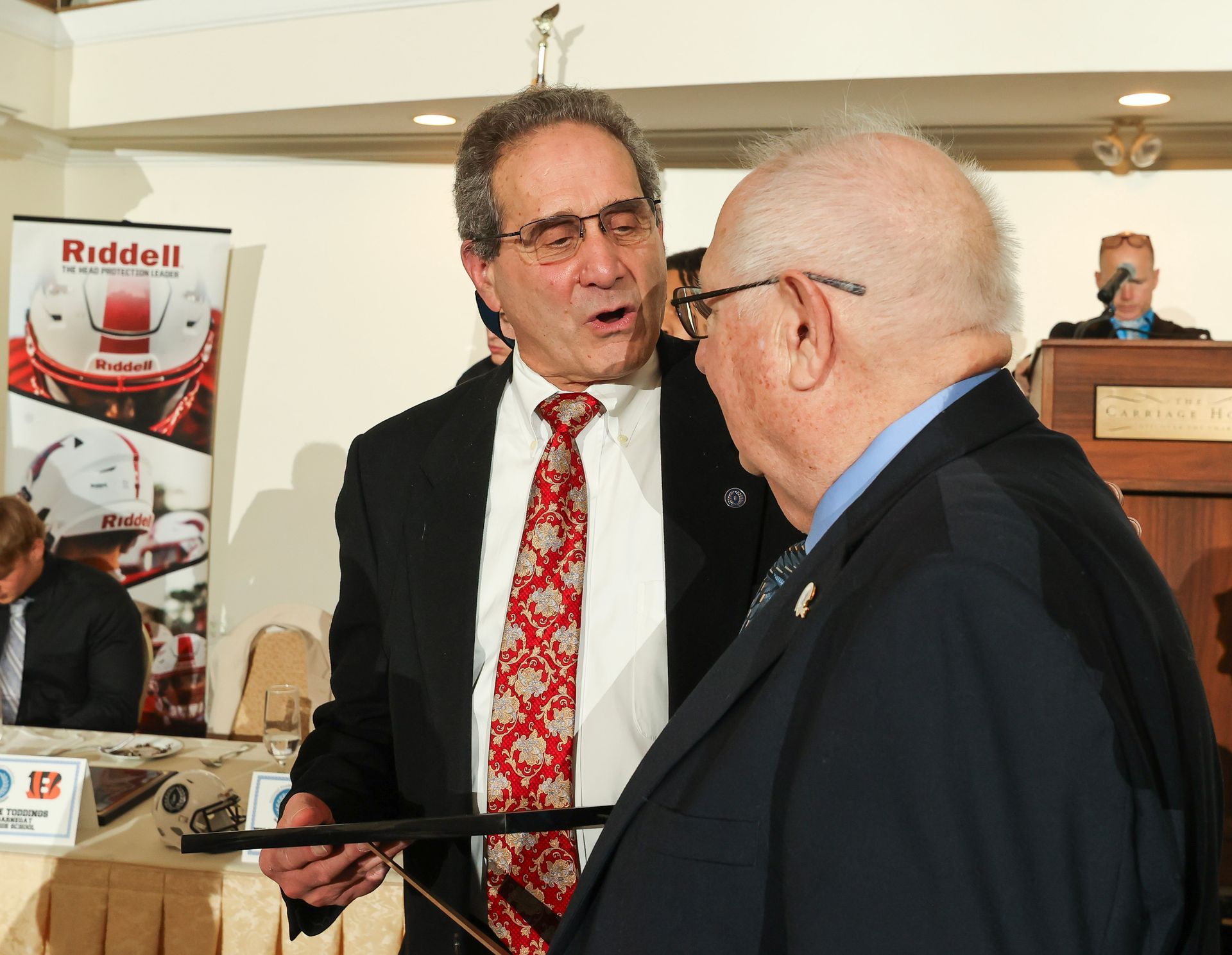 Two men are talking in front of a sign that says riddell