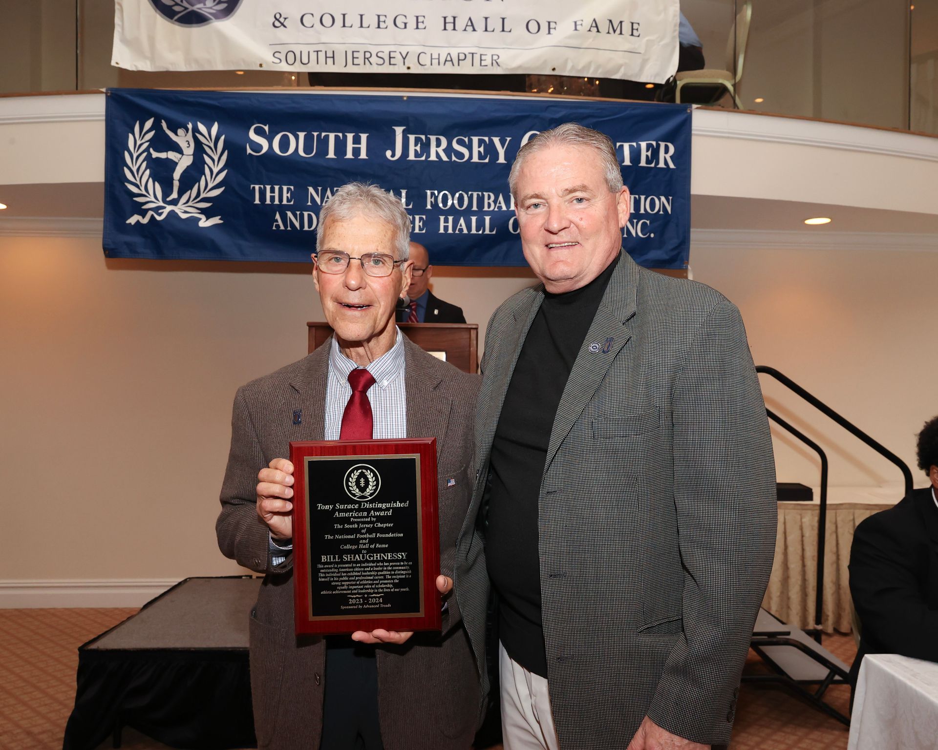 Two men standing in front of a banner that says national football foundation south jersey chapter