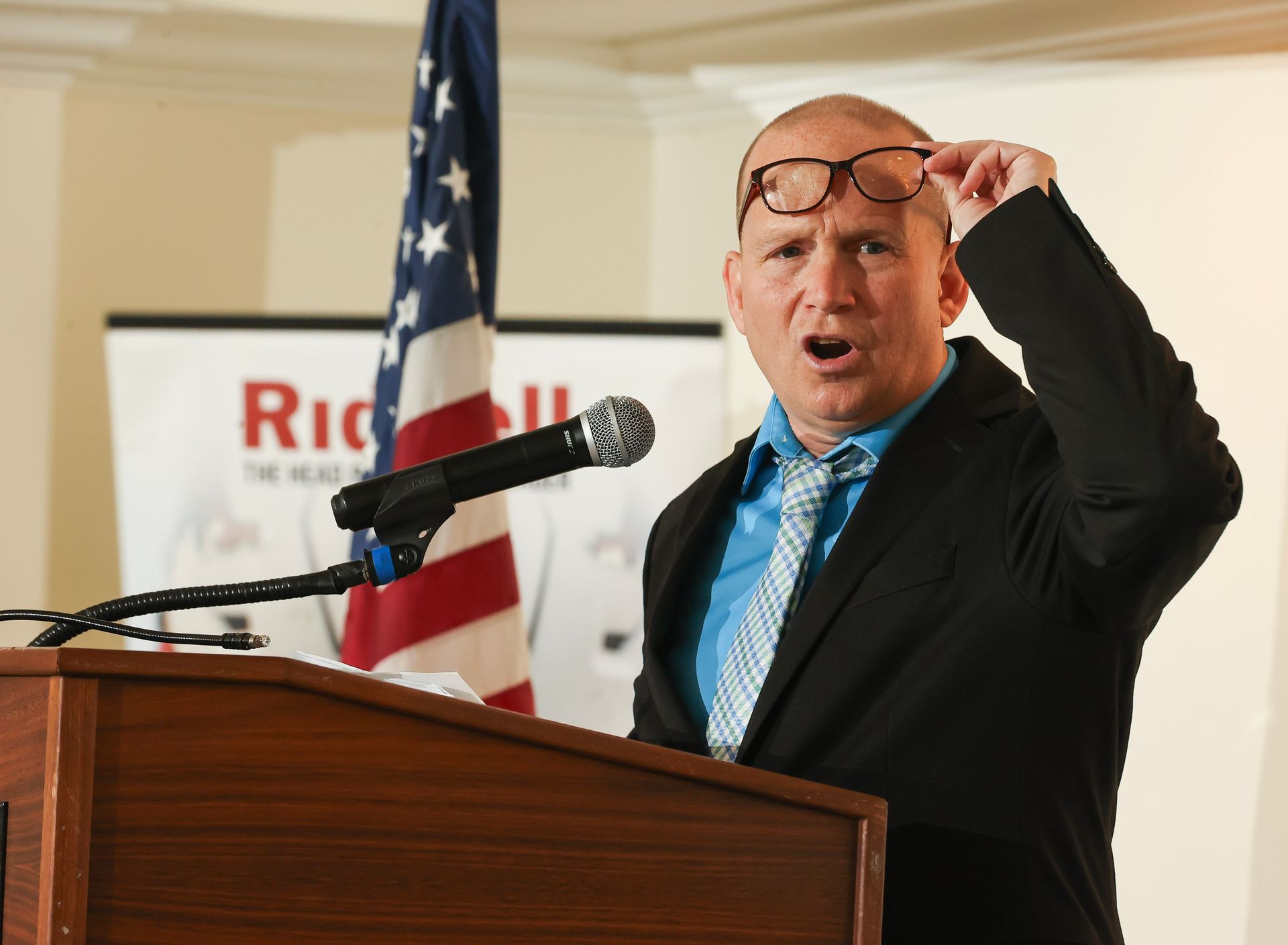 A man stands at a podium holding his glasses up