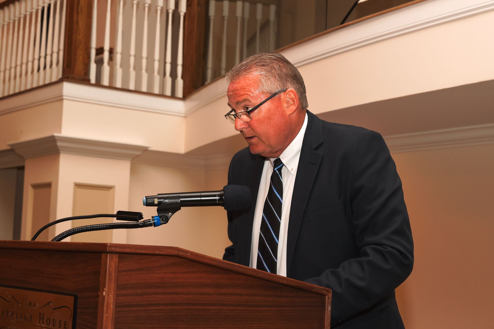 a man in a suit and tie stands at a podium speaking into a microphone