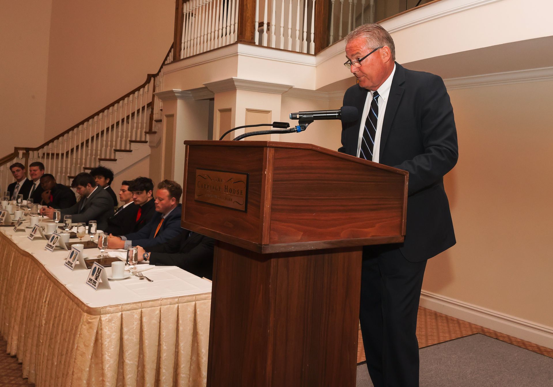 a man in a suit stands at a podium giving a speech