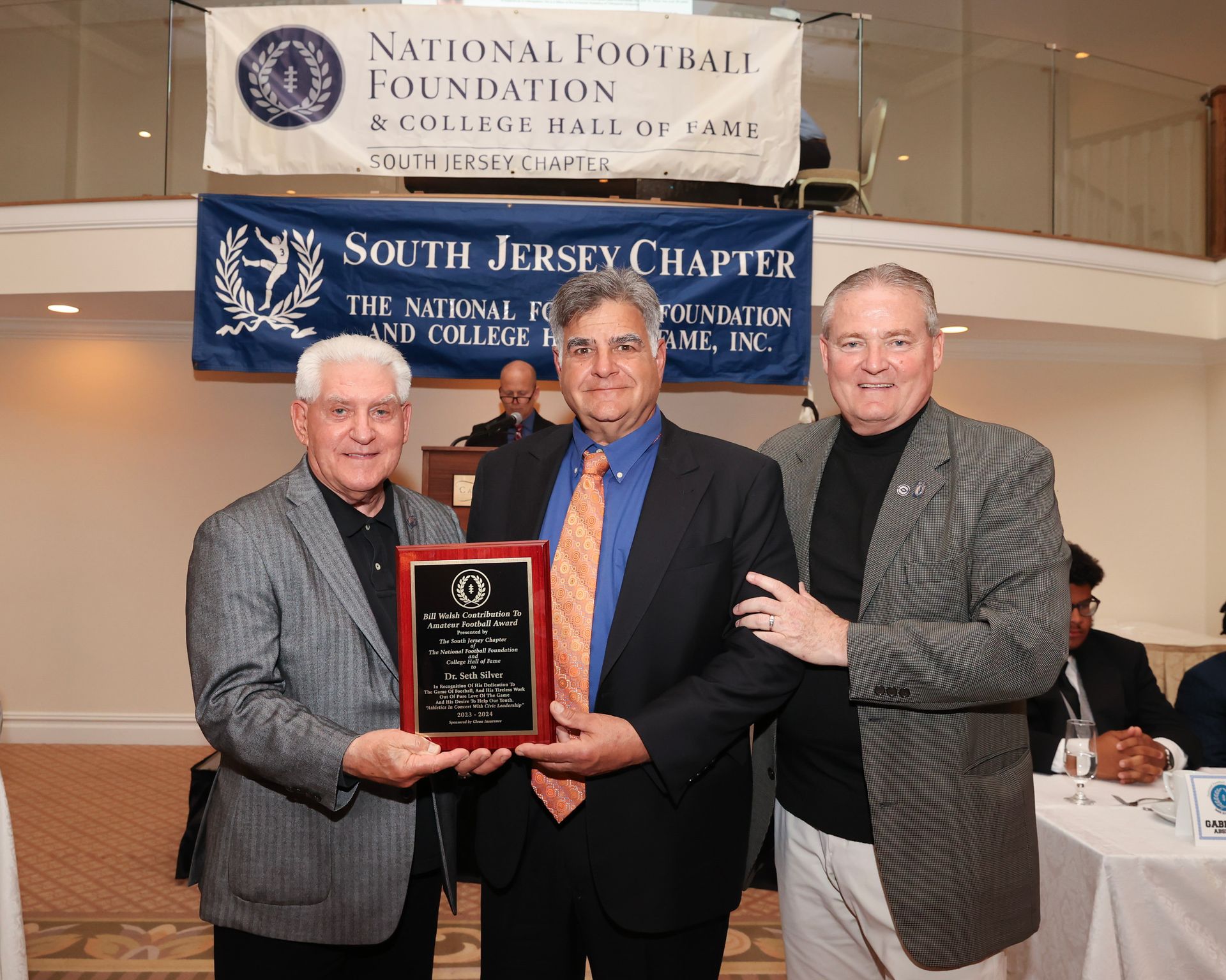 Three men standing in front of a sign that says national football foundation south jersey chapter