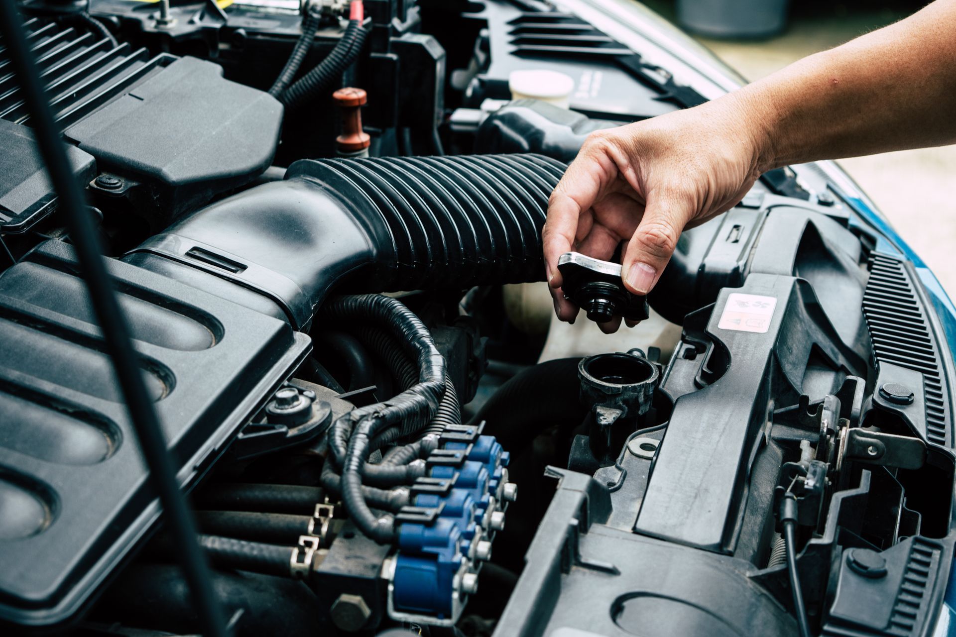 A person is holding a radiator cap under the hood of a car.