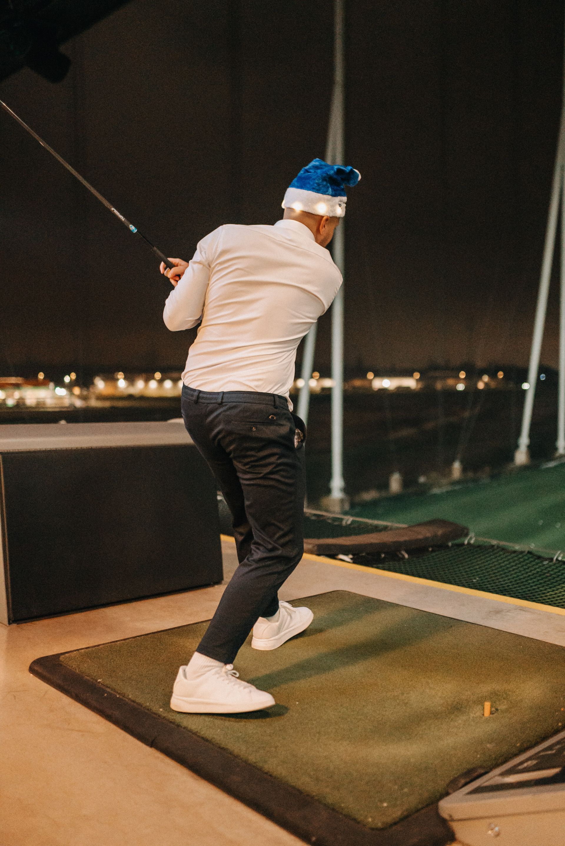Eine Person, die nachts mit einem Golfschläger spielt, eine Weihnachtsmannmütze trägt und auf einer grünen Matte steht.