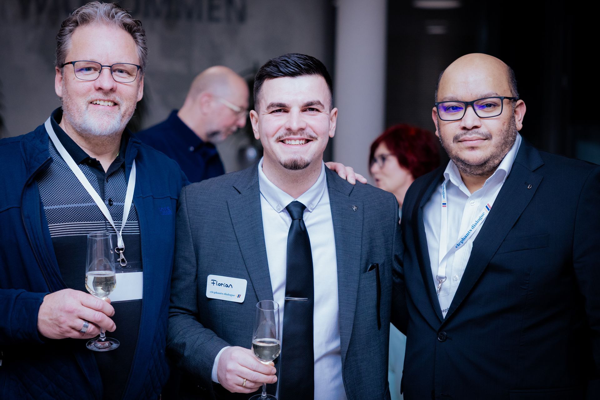Drei Männer im Haus, einer in grauer Jacke, die Arme verschränkt, zwei andere mit Brille. Einer zeigt mit dem Finger.