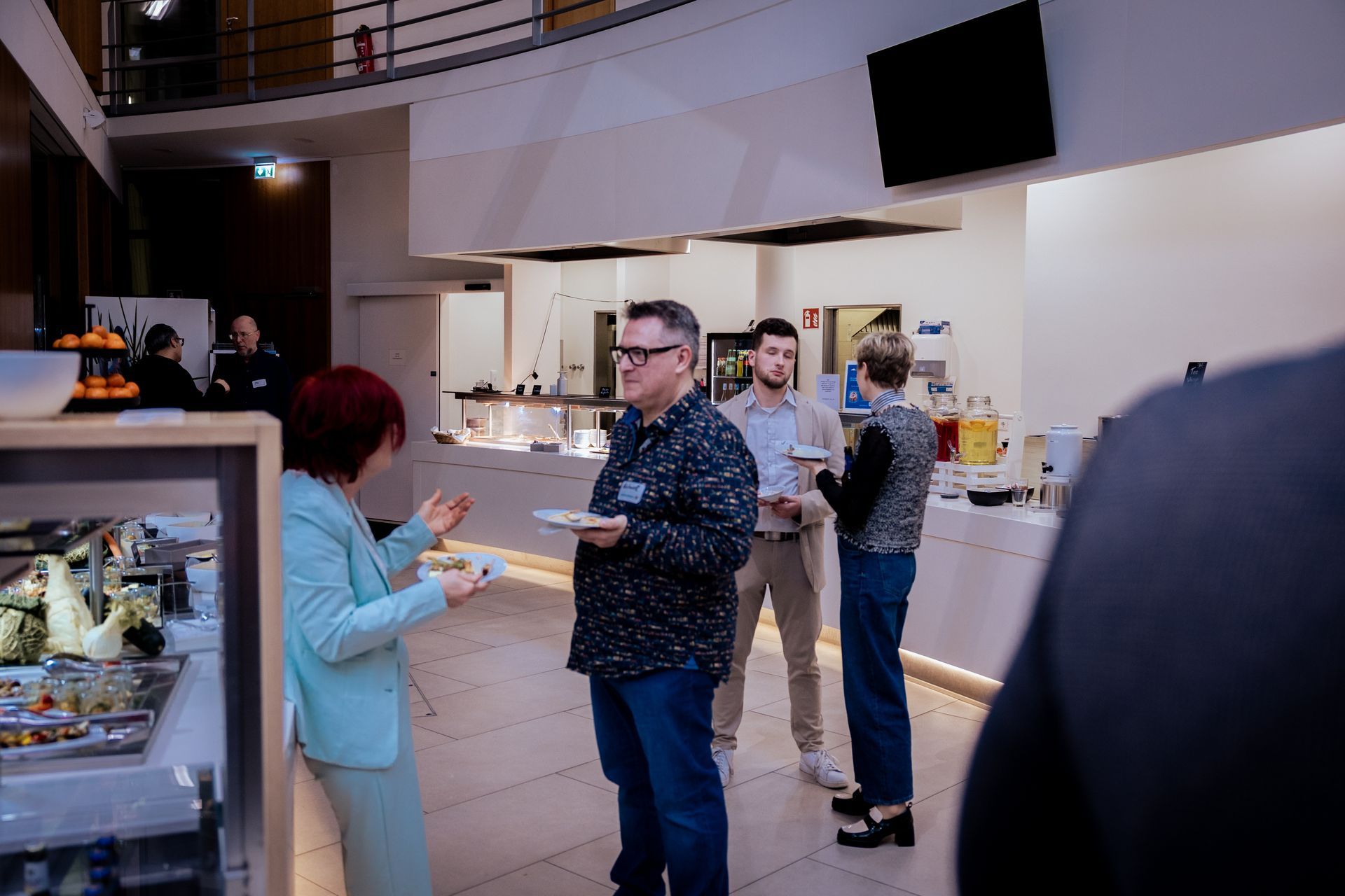 Zwei Männer essen an einem Imbissstand. Einer mit Bart lächelt. Der Tisch ist rot-weiß gemustert. Schild: „Vorspeisen“.