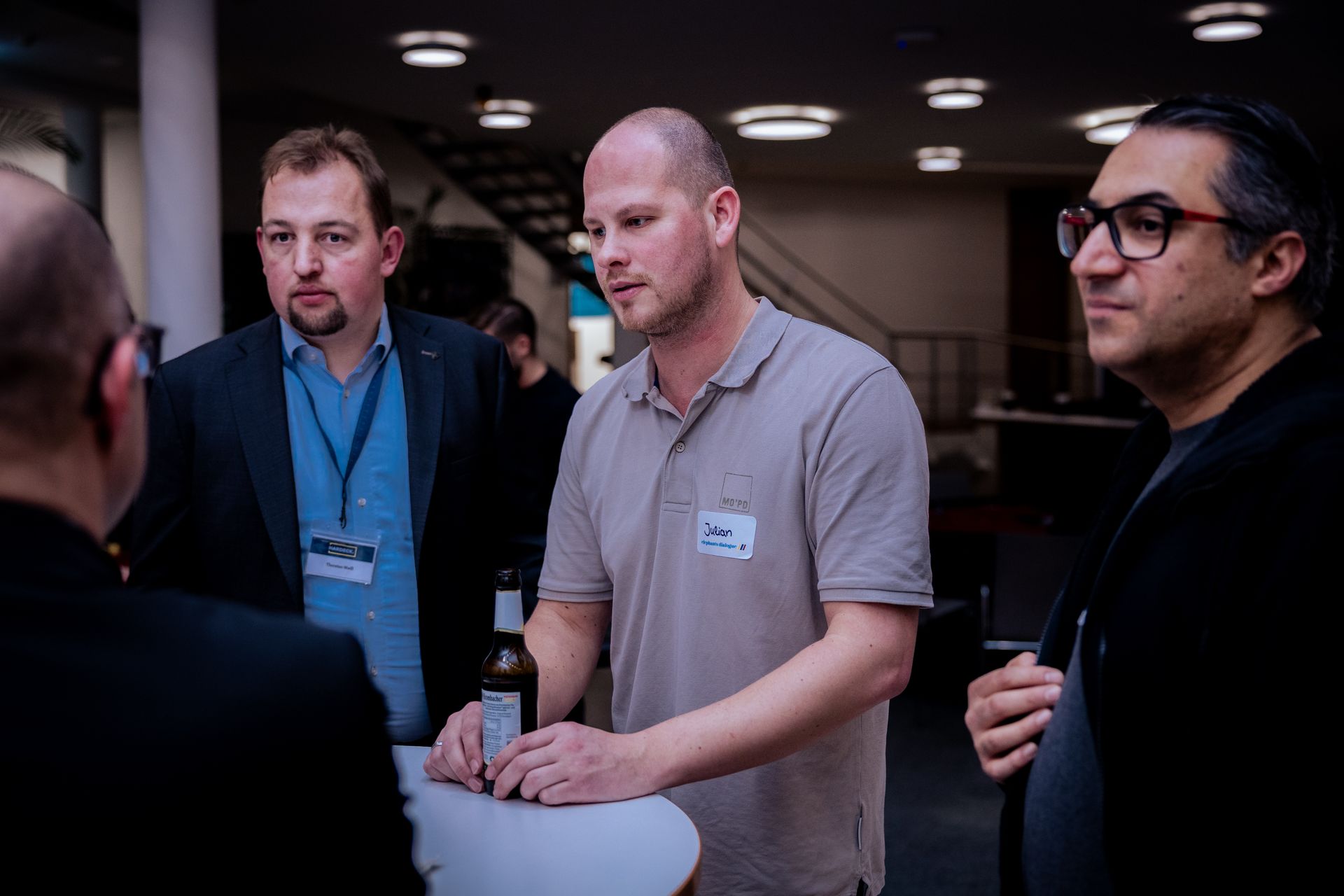 Mann mit Mikrofon, lächelnd, bekleidet mit Blazer und hellblauem Hemd, draußen bei Nacht.