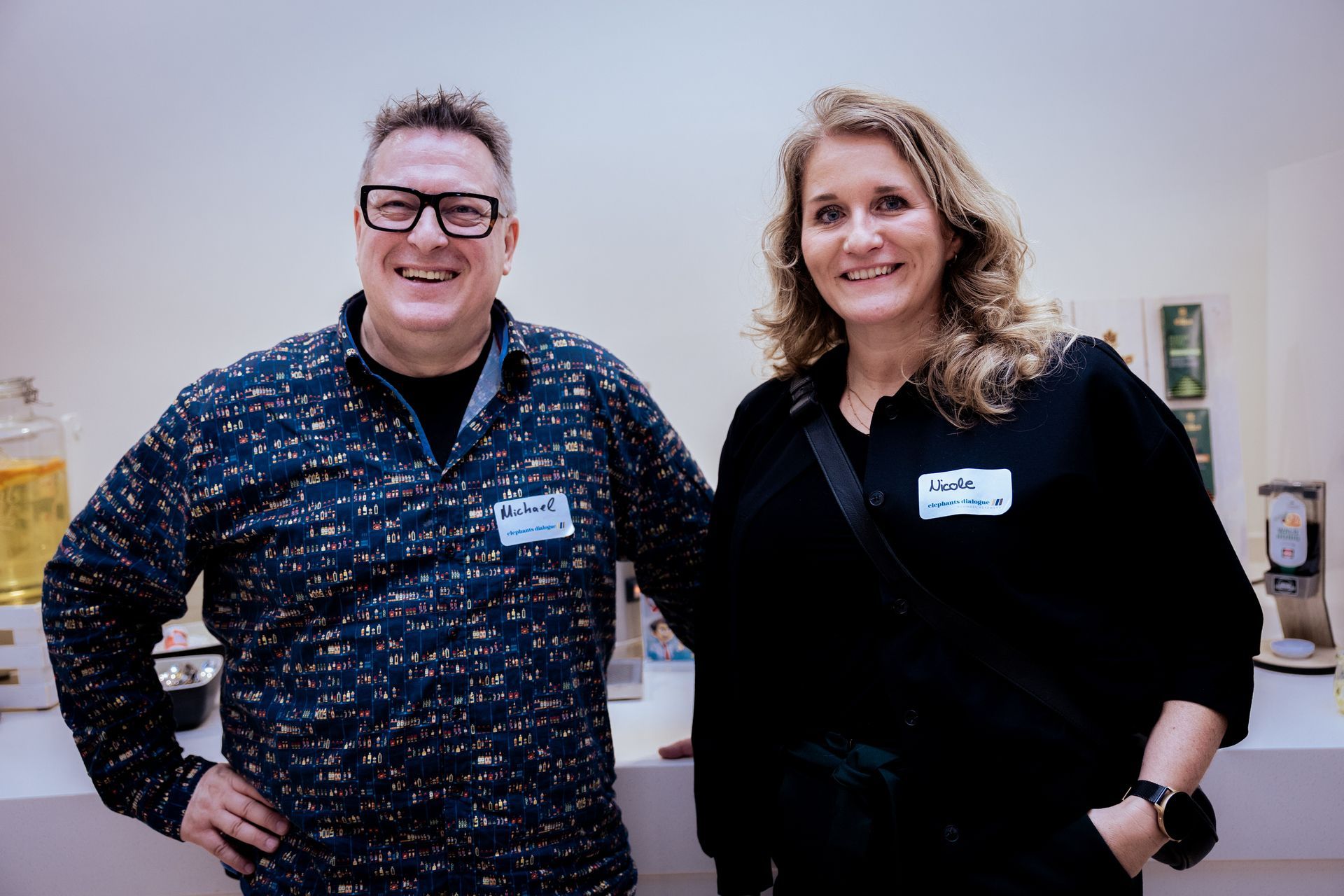 Drei Männer posieren lächelnd zusammen. Einer trägt eine braune Jacke, zwei schwarze Jacken, alle in Freizeitkleidung.