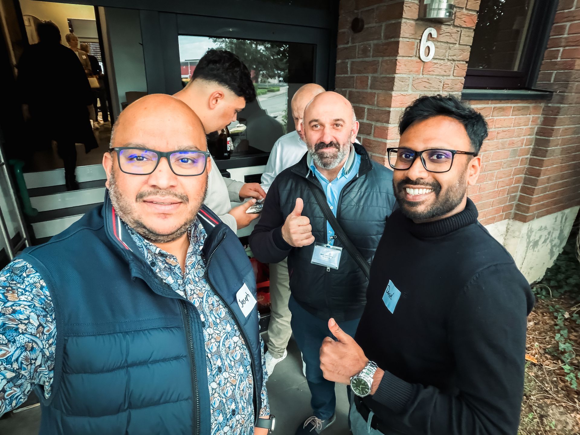 Zwei Männer, einer in einem roten, der andere in einem cremefarbenen Pullover, zeigen den Daumen nach oben. 