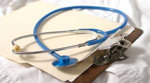 Blue stethoscope resting on a clipboard with papers, likely for a medical examination.