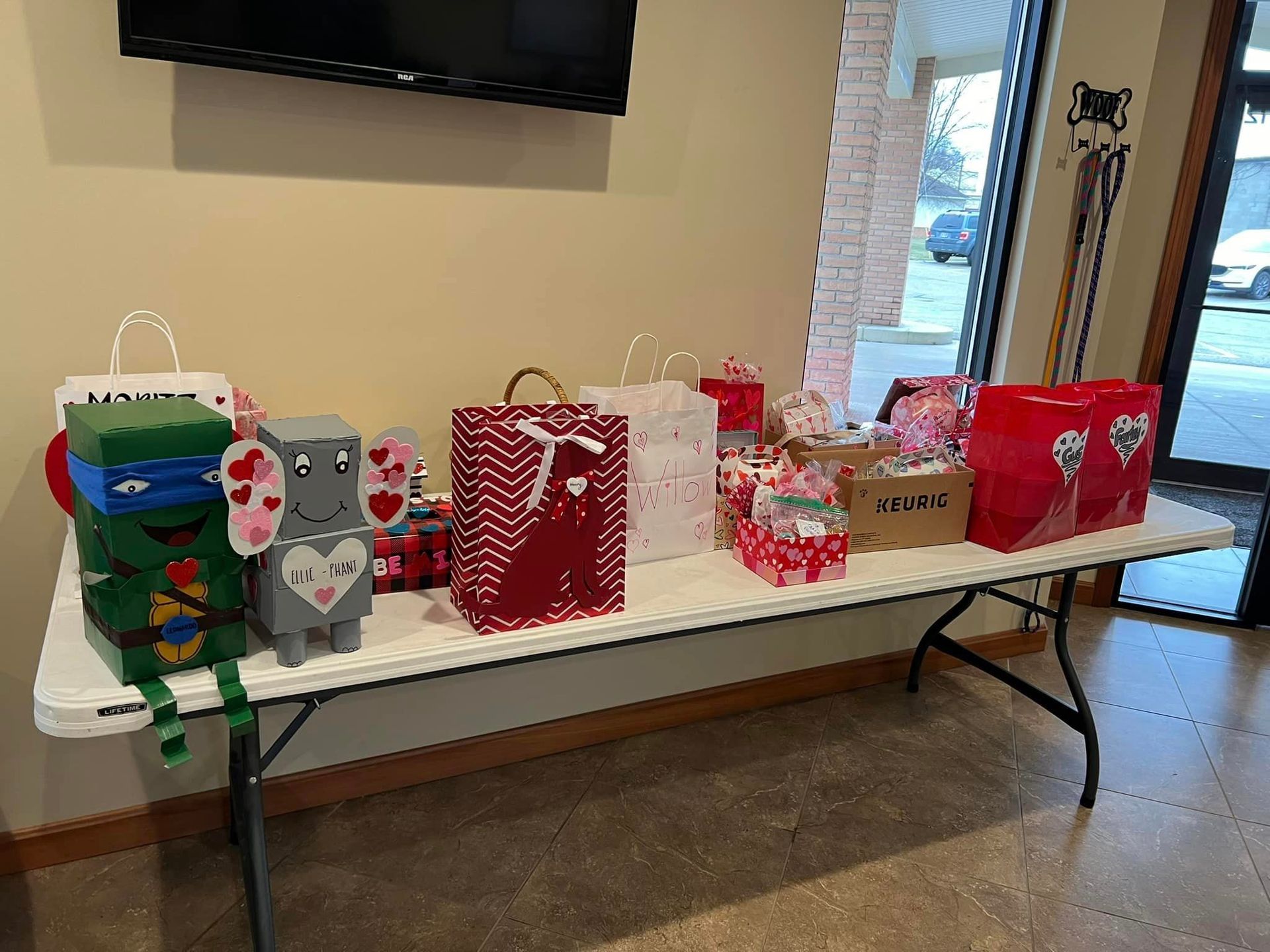 A table indoors displays Valentine's Day gifts and decorations, including gift bags and handmade animal boxes.