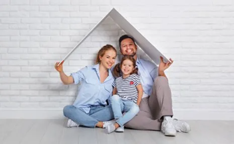 A family is sitting on the floor under a cardboard house.