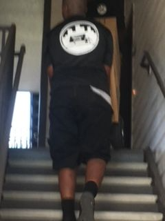 A man wearing a black shirt with a white logo on the back is walking down stairs