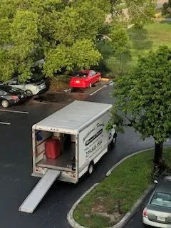 A moving truck is parked in a parking lot next to a red car.