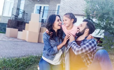 A family is sitting in front of a house with moving boxes.