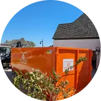 A large orange dumpster is parked in front of a house.