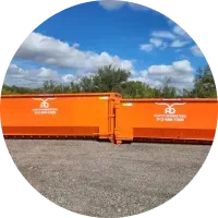 Two orange dumpsters are parked in a gravel lot.