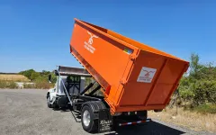 An orange dumpster is sitting on the back of a truck.