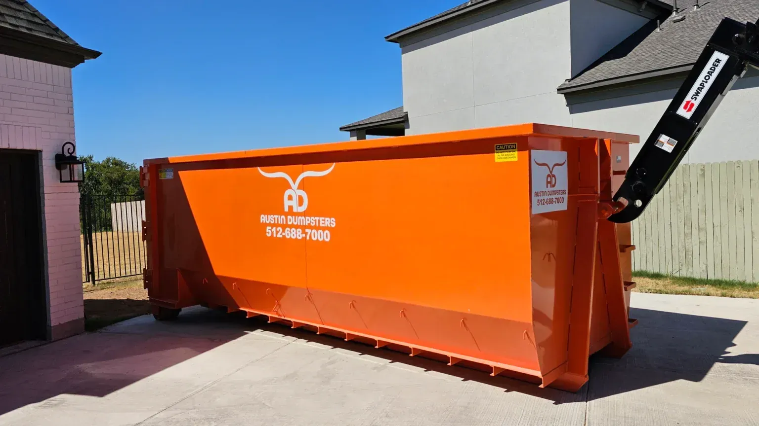 A large orange dumpster is parked in front of a house.