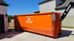 A large orange dumpster is parked in front of a house.