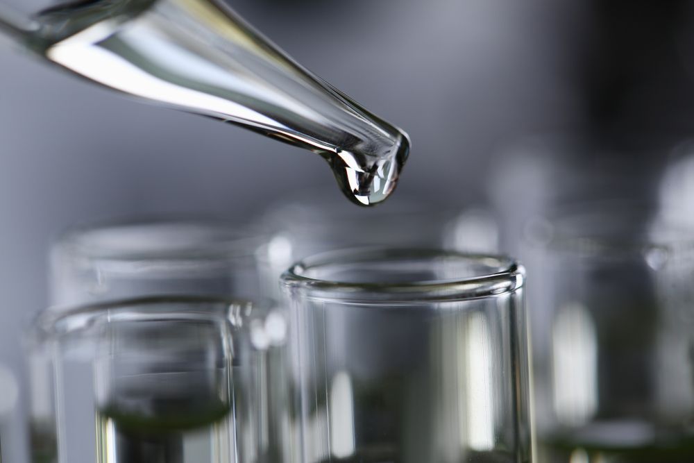 Dropper dispensing liquid into a test tube; glassware in a lab setting.