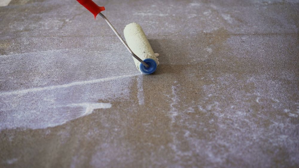 Paint roller applying white paint to a textured, brown surface.