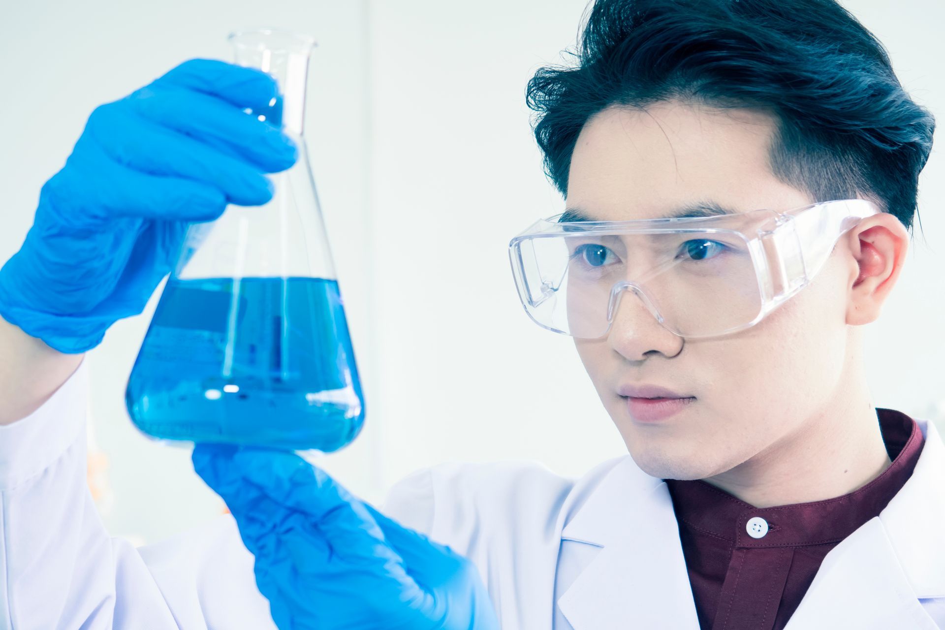 a scientist is holding a beaker with a blue liquid in it to examine its green chemistry
