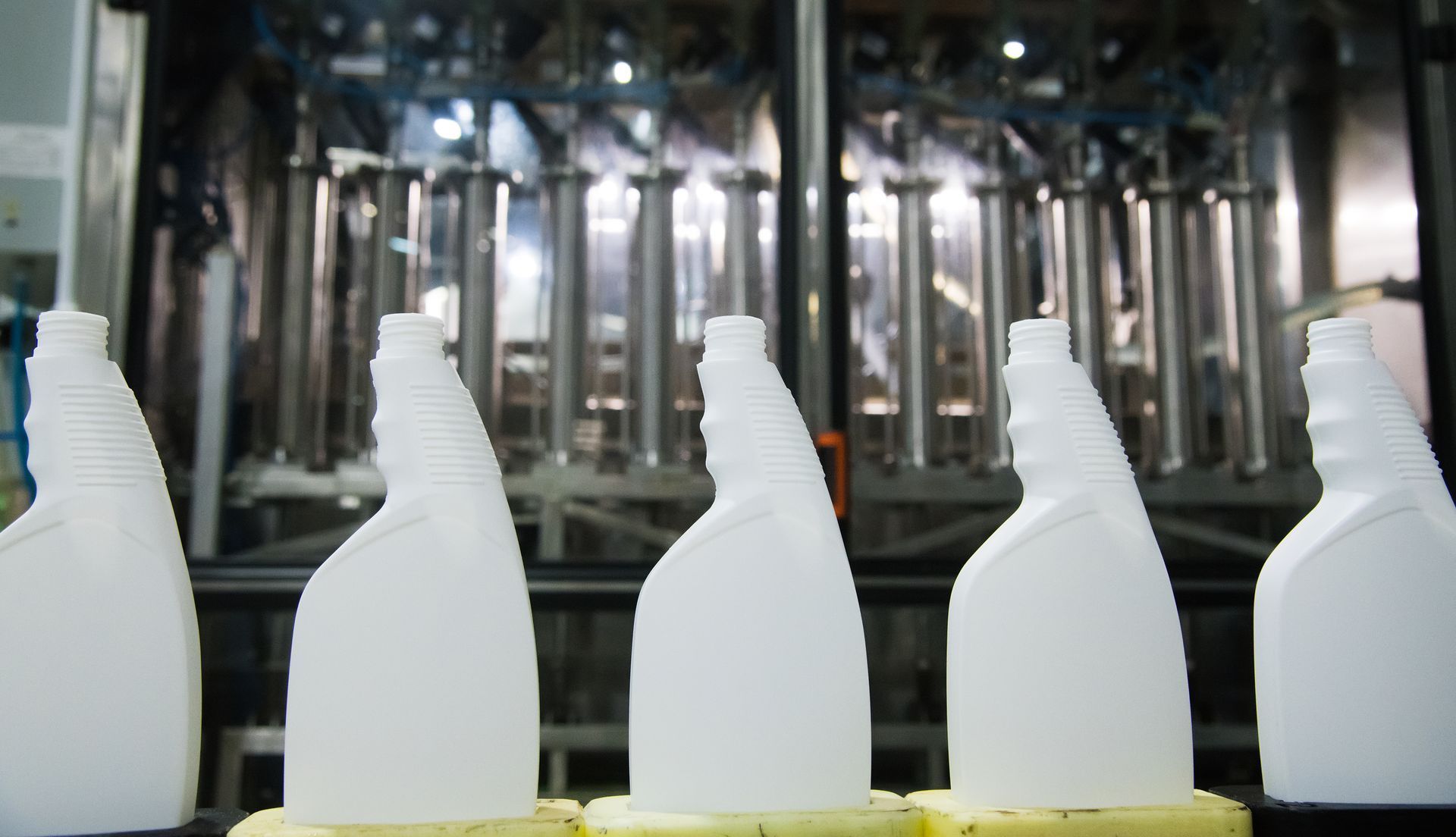 a row of white plastic bottles are lined up on a conveyor belt waiting to be filled with industrial solvents