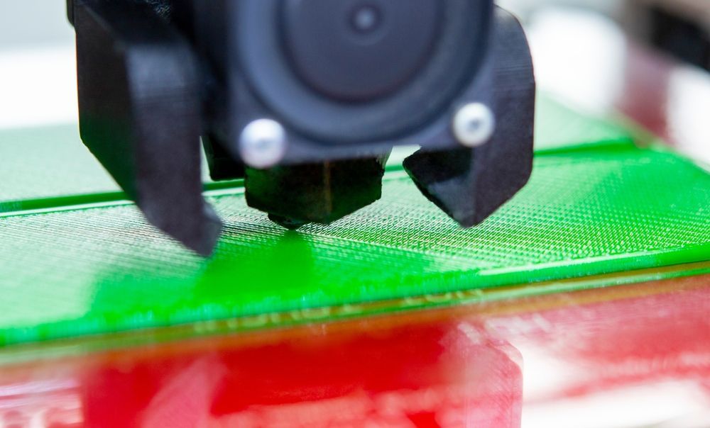 A close up of a 3d printer printing a green object.