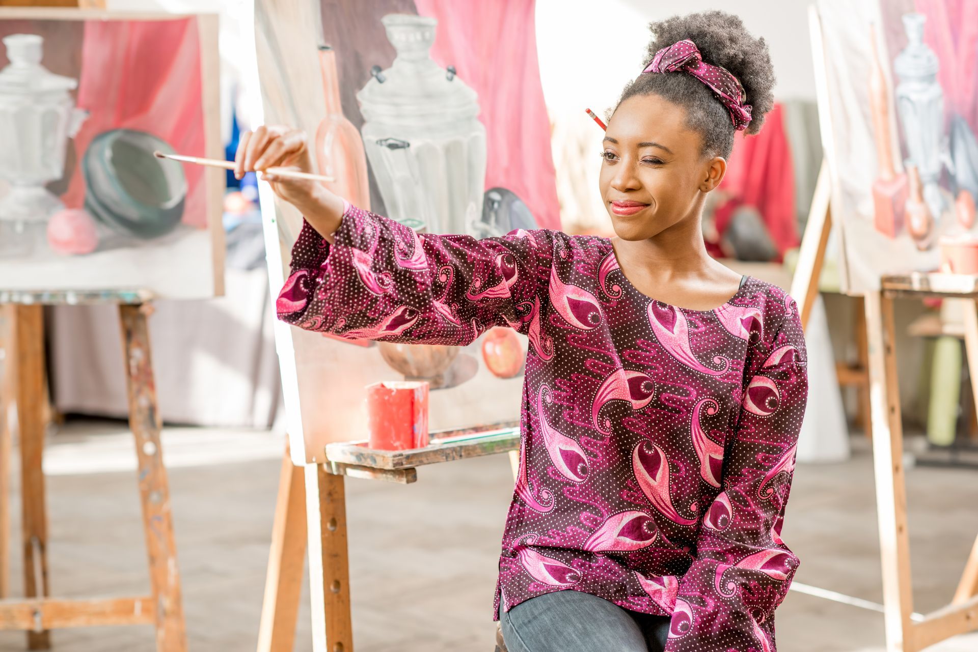 A young African American woman sizes something out of frame with her paintbrush for her oil painting class, she's concerned about the differences between mineral spirits vs acetone