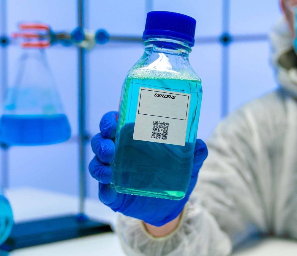 Gloved hand holding a blue liquid lab bottle in a laboratory setting