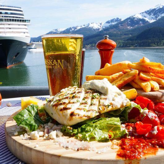 Photo of The Hangar's grilled halibut & fries with a cold beer. Cruise ship and snow capped mountains in the background
