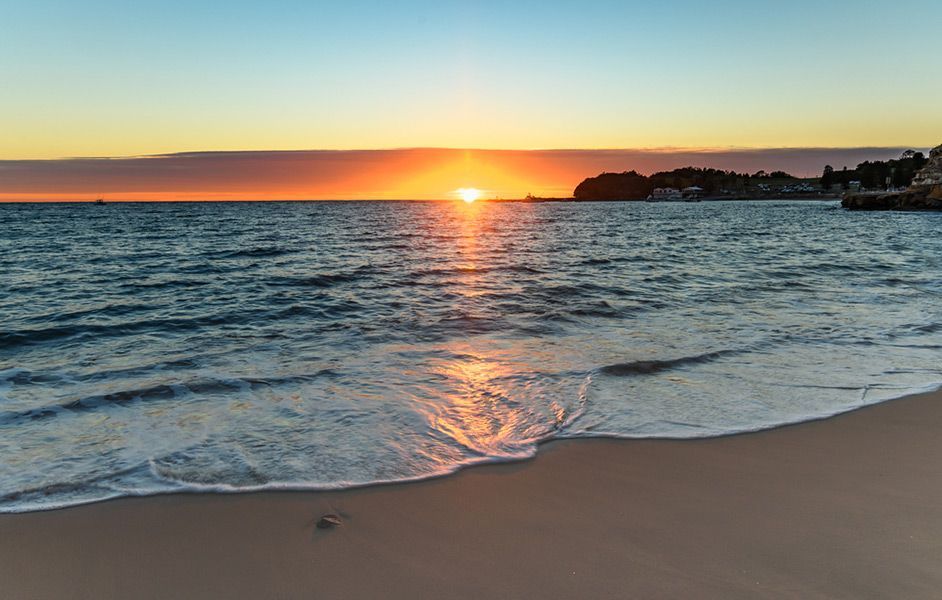The Sun Is Setting Over the Ocean and The Waves Are Crashing on The Beach — Maison Property Management in Central Coast, NSW