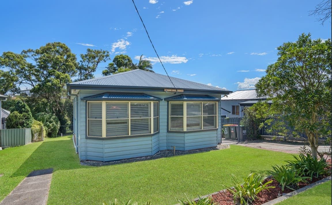 A small house with a lot of windows is sitting on top of a lush green lawn — Maison Property Management in Mayfield, NSW