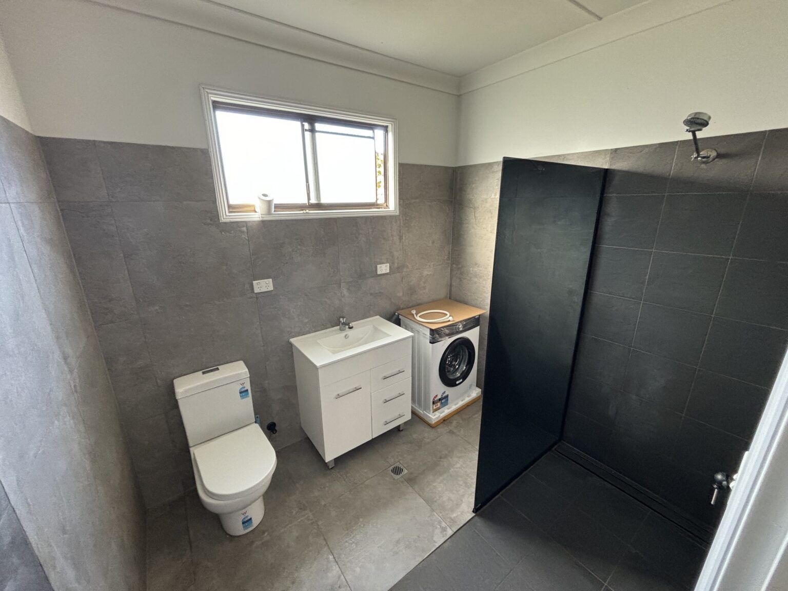 A bathroom with a toilet , sink , washer and dryer — Maison Property Management in Mayfield, NSW