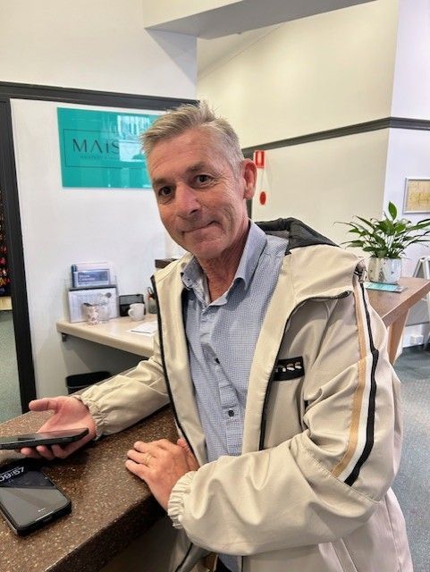 A Man in a white Jacket is Standing at a Counter Holding a Cell Phone.