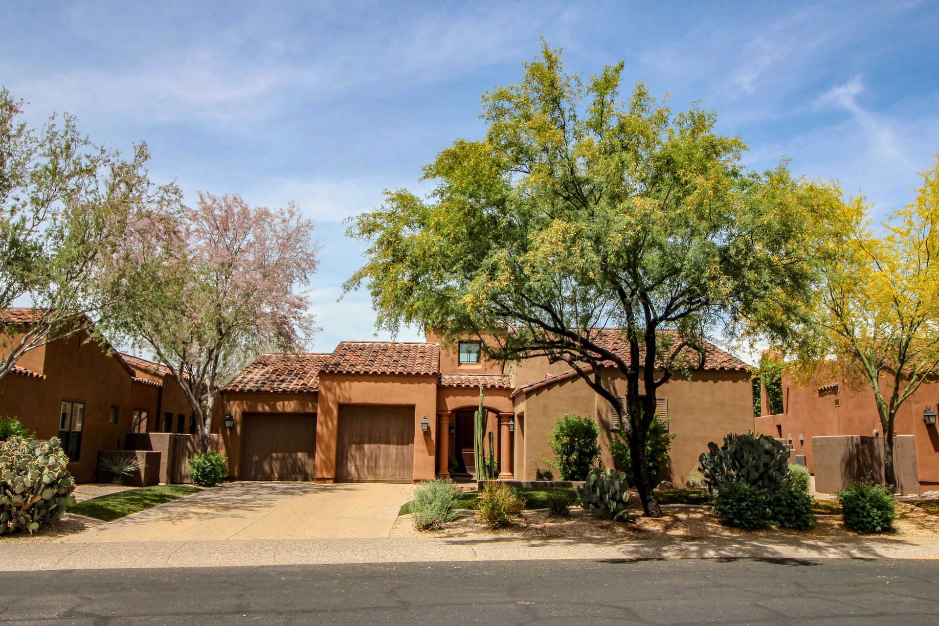 Spanish-style home with tan stucco, clay tile roof, and desert landscaping under a blue sky.
