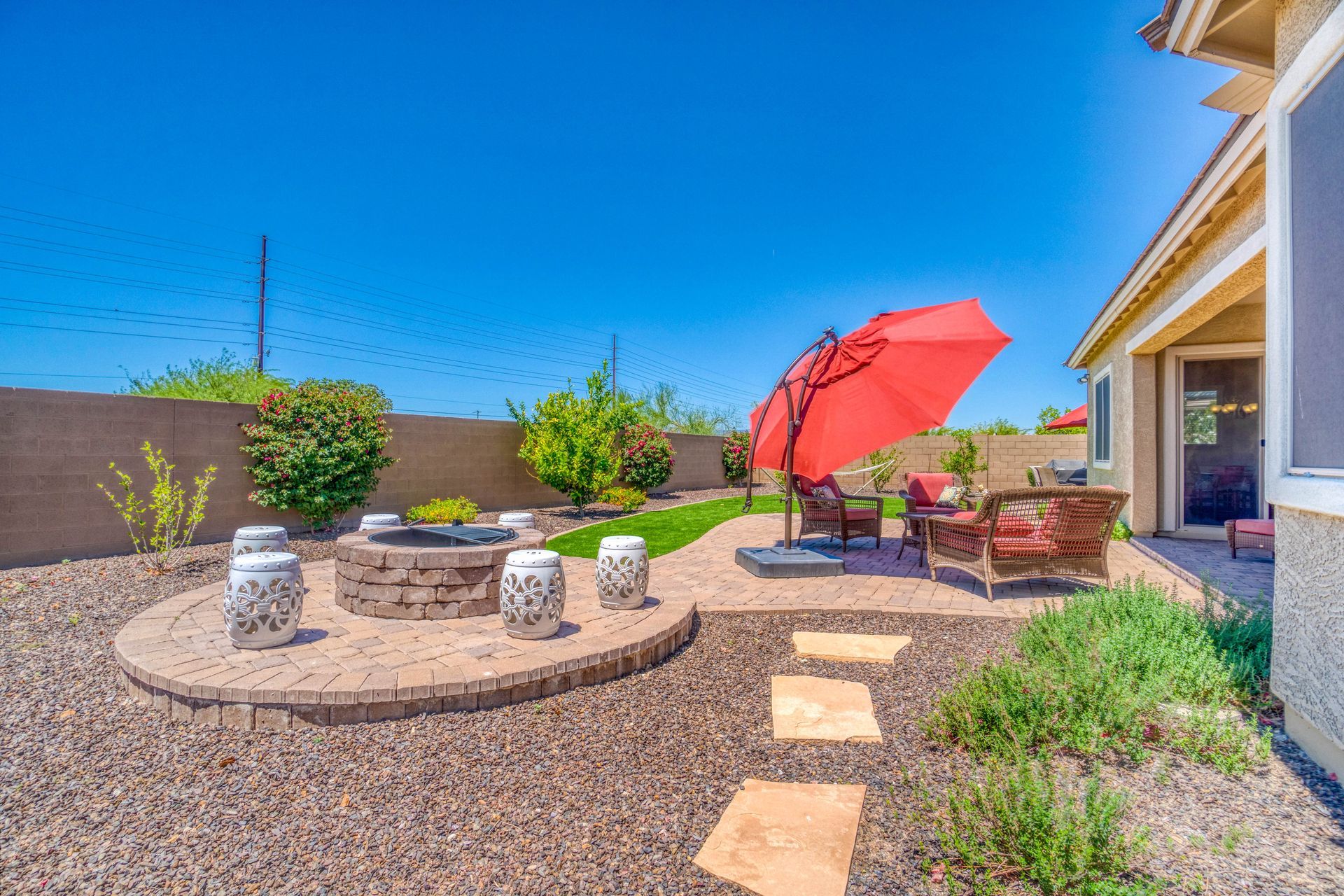 Backyard with fire pit, patio furniture, and red umbrella under a bright blue sky.