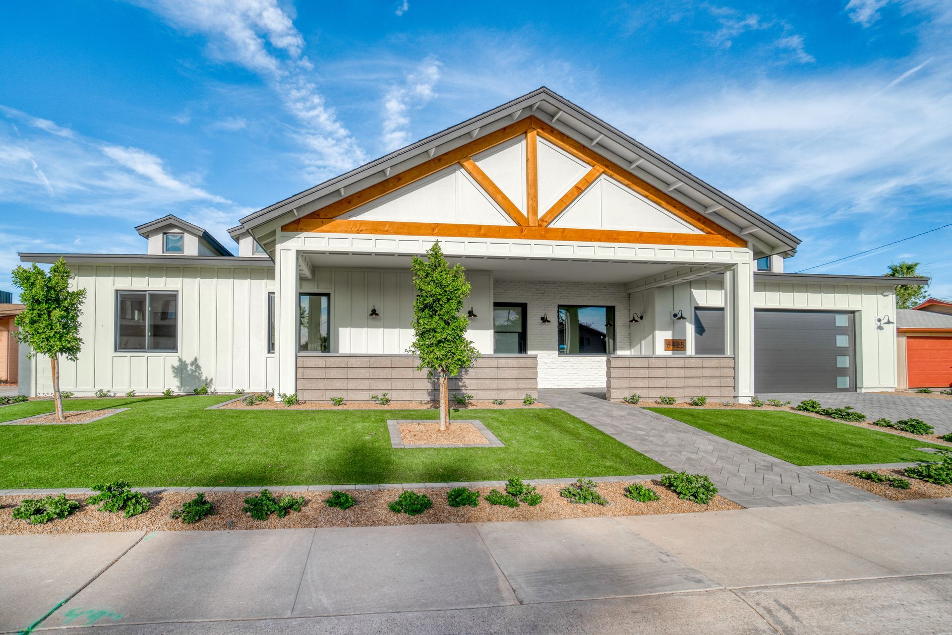 White modern home with a gabled roof, a front porch, and a gray garage door.