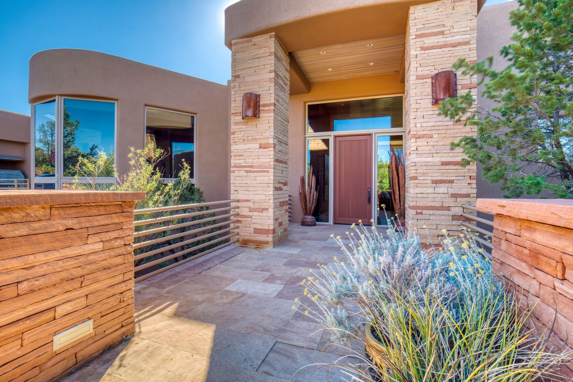 Tan stucco home with brick columns, arched roof, and tiled pathway leading to a brown door.