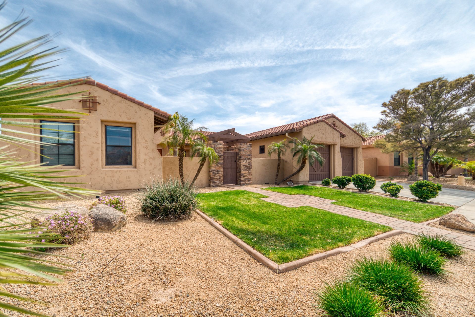 Tan stucco house with a tiled roof and desert landscaping under a blue sky.