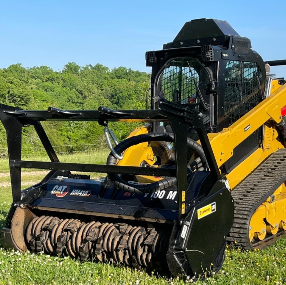 Yellow skid steer with black brush cutter on a grassy field.