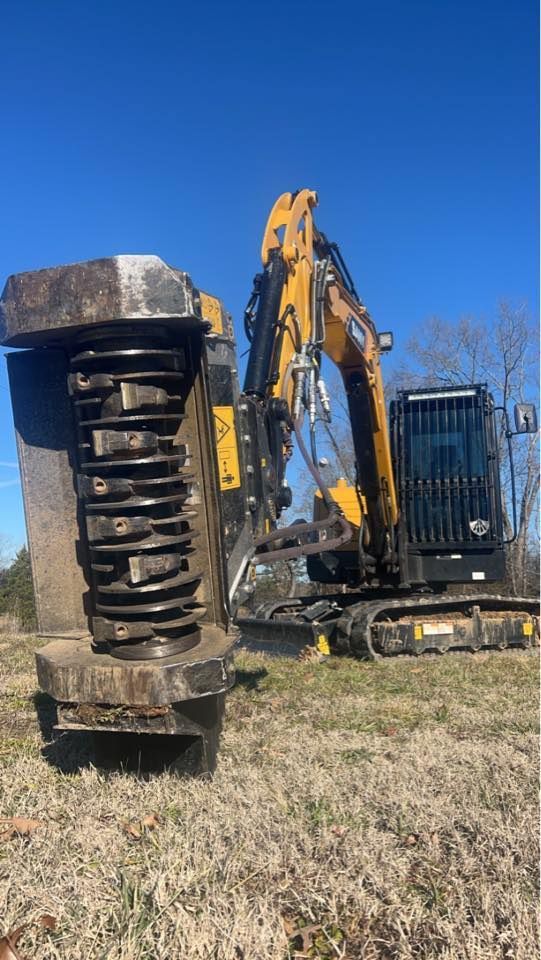 Yellow excavator with a brush cutter attachment in a field.