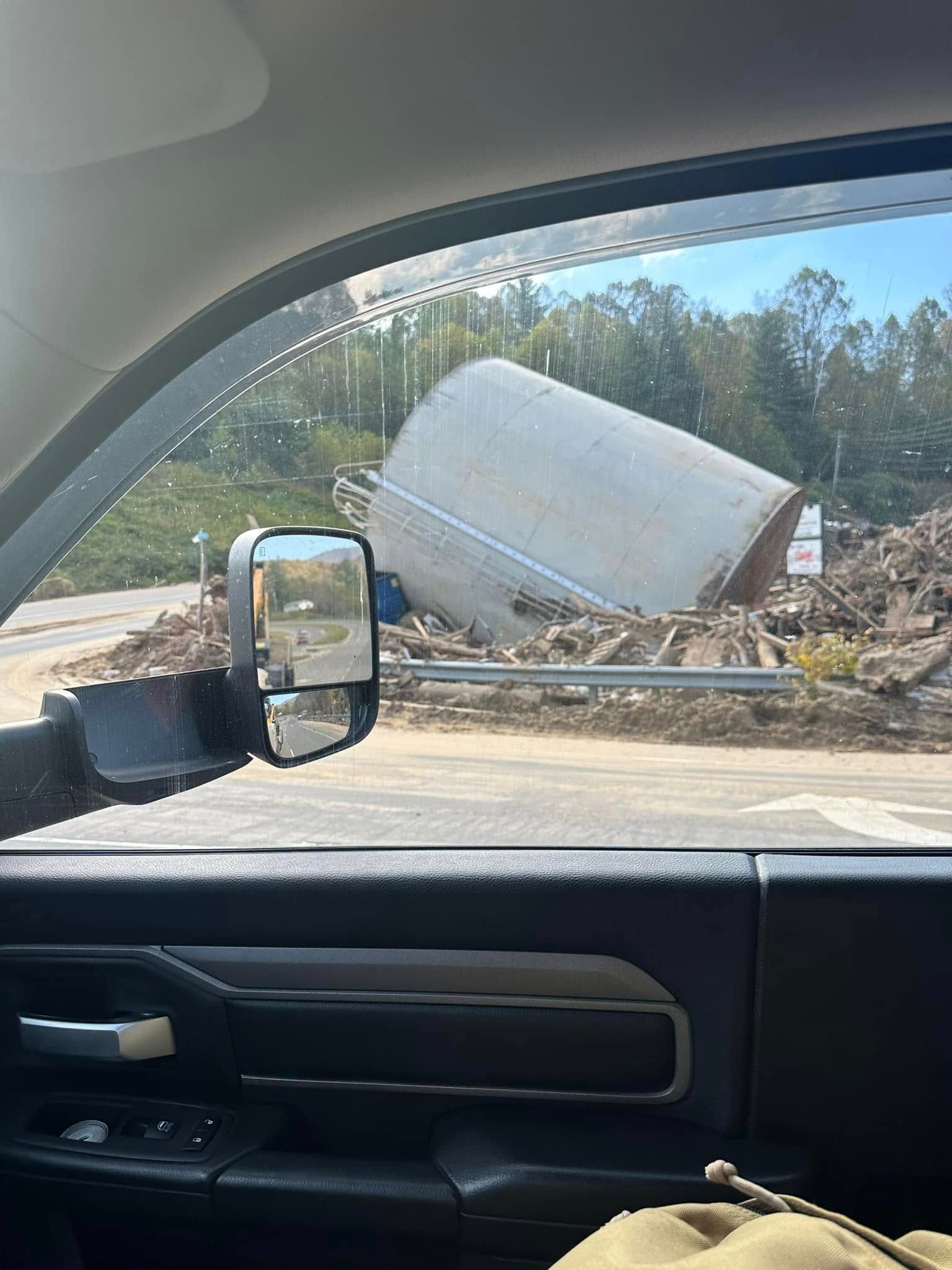 A large cylindrical structure on its side amidst construction debris; seen from a vehicle's window with a side mirror.