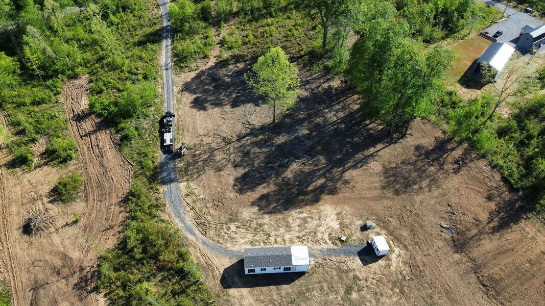 Aerial view of a house with a curved driveway, surrounded by trees and cleared land.