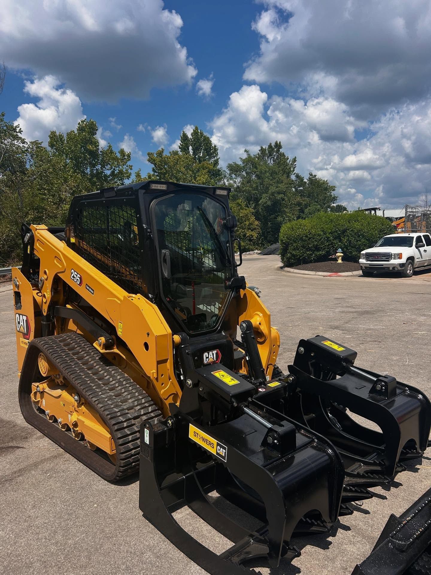 Yellow and black skid steer with forestry mulcher attachment, parked outside on a sunny day.
